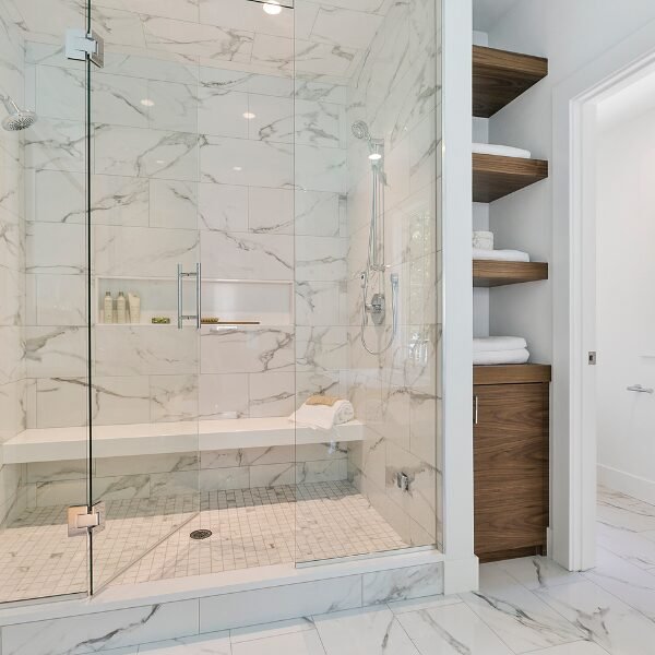 Classy Mint Hill master shower with decorative tile, long bench, and glass entry.